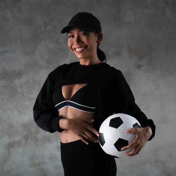 コンクリートの背景の上に隔離されたサッカーボールを保持するスポーツ服を着た美しい若い笑顔の女性の肖像画 — ストック写真