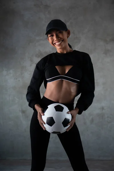 コンクリートの背景の上に隔離されたサッカーボールを保持するスポーツ服を着た美しい若い笑顔の女性の肖像画 — ストック写真