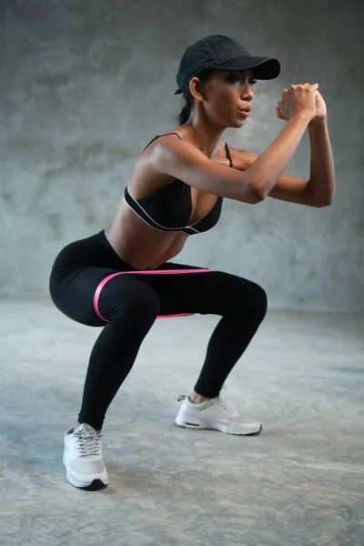 健康美丽的女人在健身房与阻力乐队一起锻炼 女运动员为下身的肌肉做蹲下练习 — 图库照片