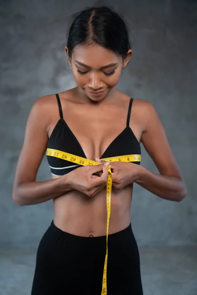 Portrait of fitness beautiful and smiling female model with measuring tape posing at the fitness gym