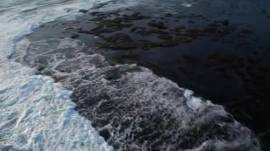 Bali, Endonezya siyah kum plaja karşı kayalar üzerinde ezici güzel deniz dalgaları üzerinde uçan hava drone görünümü