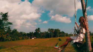 Tropikal palmiye ağaçları arka plan ile güzel pirinç tarlaları üzerinde sallanan beyaz elbiseli kadının havadan yan görünümü