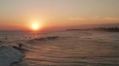 Güzel altın gün batımı arka planında sörf yapan insanların hava aracı görüntüsü.