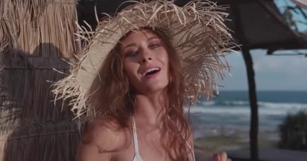 美丽的晒黑的健身女人在比基尼姿势与草帽附近的海滩 视频在慢动作 — 图库视频影像