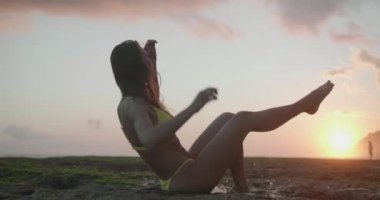 Gün batımında deniz suyunda oynayan sarı bikinigüzel tabaklanmış fit mutlu kadın - yavaş çekimvideo