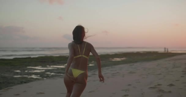 黄色のビキニランニングで美しい日焼けフィット幸せな女性は 日没時にビーチで踊る スローモーションでビデオ — ストック動画