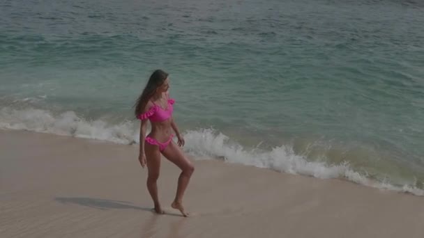 ビーチで自由な時間を過ごすピンクのビキニで美しい日焼けしたフィットネス女性 スローモーションでビデオ — ストック動画