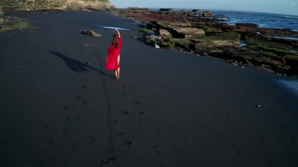 黒い輝く砂浜でビキニと赤い全体的なポーズで美しい官能的な女性の空中ドローンビュー — ストック動画