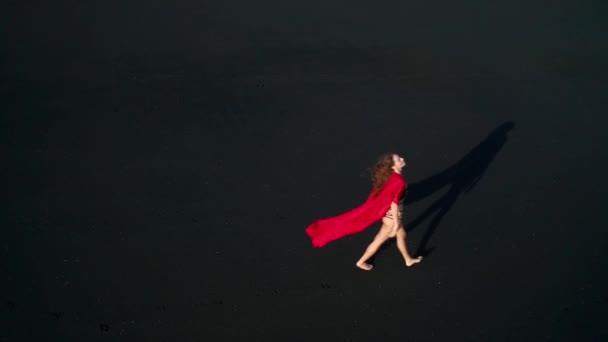 黒い輝く砂浜でビキニと赤い全体的なポーズで美しい官能的な女性の空中ドローンビュー — ストック動画