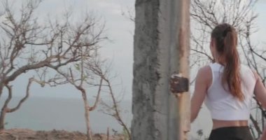 Gün doğumunda deniz kıyısındaki kayalıkta koşan genç çekici kadının geri görünümü - yavaş çekimde video