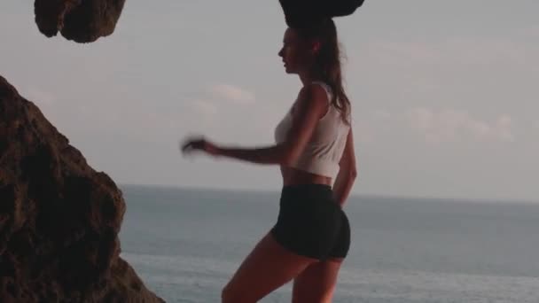 日の出の海岸の崖で朝ジョギングの後に休憩を取る若い魅力的な女性 — ストック動画