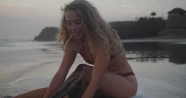 Turuncu bikinigüzel mutlu kız gün batımında siyah plajda eğlenmek - yavaş hareket video