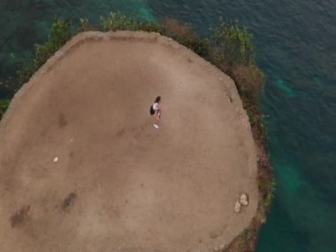 Gün doğumunda deniz kıyısındaki kayalıkta direniş gücü bandı ile egzersiz genç çekici kadın havadan drone görünümü