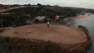 Gün doğumunda deniz kıyısındaki kayalıkta egzersiz genç çekici kadın havadan drone görünümü