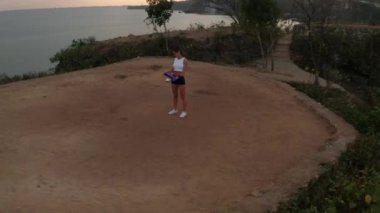 Gün doğumunda deniz kıyısındaki kayalıkta direniş gücü bandı ile egzersiz genç çekici kadın havadan drone görünümü