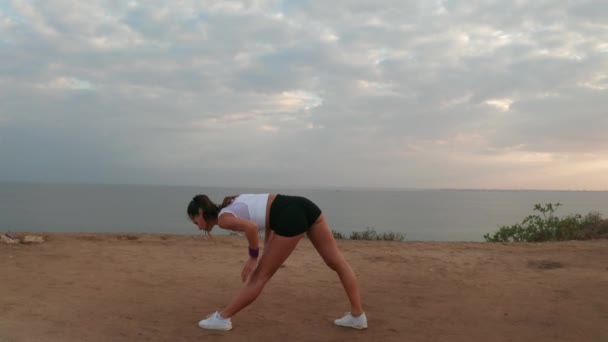 日の出時に海岸の崖で運動する若い魅力的な女性の空中ドローンビュー — ストック動画
