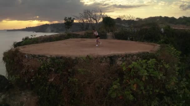 日の出時の海岸崖で抵抗力帯で運動する若い魅力的な女性の空中ドローンビュー — ストック動画