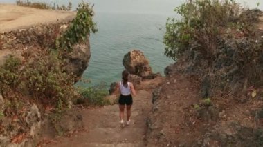 Sabahtan sonra deniz kıyısında güneş doğarken koşuya çıkan çekici genç bir kadının hava aracı görüntüsü.