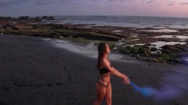 Gün batımında siyah kum plajda renkli duman ile bikini dans güzel şehvetli kadın havadan drone görünümü