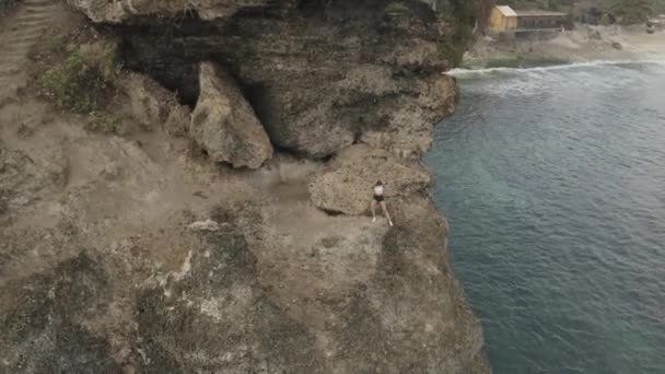 黎明时分 年轻迷人的女子在海滨悬崖上慢跑后休息的空中无人驾驶图像 — 图库视频影像
