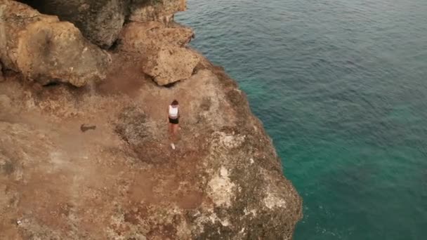 黎明时分 年轻迷人的女子在海滨悬崖上慢跑后休息的空中无人驾驶图像 — 图库视频影像