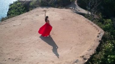 Güneşli yaz gününde deniz kıyısındaki kayalıkta poz veren kırmızı elbiseli güzel kadının havadan drone görünümü