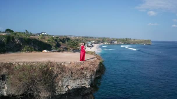 在阳光明媚的夏日 身着红色礼服的漂亮女人在海边悬崖上摆姿势的无人机空中视图 — 图库视频影像