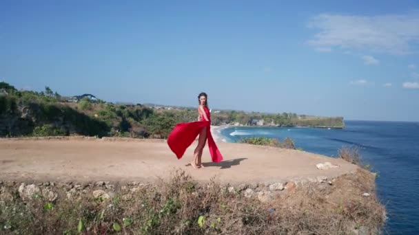 晴れた夏の日の間に海岸の崖にポーズ赤いドレスで美しい女性の空中ドローンビュー — ストック動画