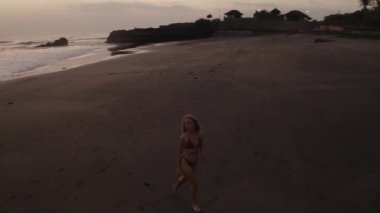 Gün batımında siyah plajda dinlenen bikini güzel kız havadan drone görünümü