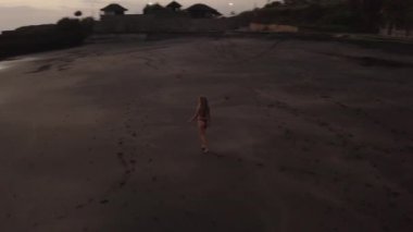 Gün batımında siyah plajda dinlenen bikini güzel kız havadan drone görünümü