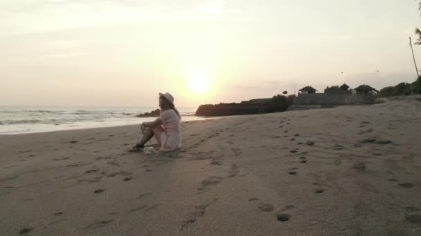 美しい夏の夕日の間に砂浜でリラックスドレスと帽子のかなり幸せな女の子 — ストック動画