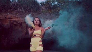 Gün batımı nda siyah kum plajda renkli duman ile neon kıyafeti şehvetli esmer kız - yavaş hareket video
