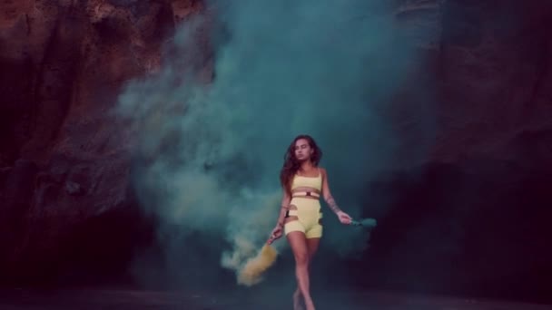 日没時に黒い砂浜で色付きの煙とネオンの衣装で官能的なブルネットの女の子 スローモーションでビデオ — ストック動画