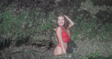 Kırmızı bikini ve üst kayalara yakın deniz suyunda poz şehvetli esmer kız - yavaş hareket video