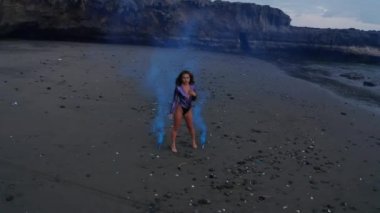 Gün batımında siyah kum plajda renkli duman ile poz mor bodysuit şehvetli esmer kız