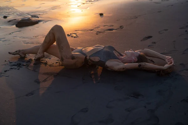 美丽的性感女人在闪闪发光的泳装在黑色沙滩在惊人的金色日落中摆姿势 — 图库照片