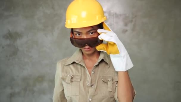 有吸引力的年轻女孩建设者与油漆辊制服 防护眼镜和手套微笑在混凝土墙背景 — 图库视频影像