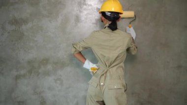 Üniforma, kask, koruyucu gözlük ve eldiven beton duvar painitng boya rulo ile kız oluşturucu geri görünümü
