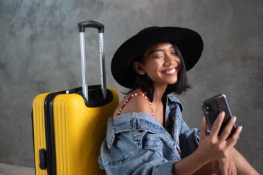 Gülümseyen genç Asyalı kadının portresi, cep telefonuyla beton duvara izole edilmiş selfie fotoğrafı çekiyor. İnsanlar yaşam tarzı, seyahat konsepti