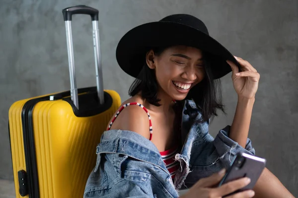微笑的年轻亚洲妇女与行李做自拍照片与她的手机隔离在混凝土墙上的肖像 人的生活方式 旅游理念 — 图库照片