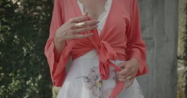木製のドアゲートの近くに花と庭でボレロを脱ぐ花のドレスを着た女性のクローズアップボディ スローモーションでビデオ — ストック動画