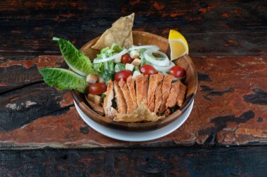 Kırsal ahşap mutfak masasında ızgara tavuklu Yunan salatası.