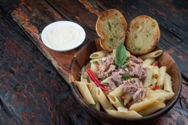 Ton balıklı makarna, sarımsaklı ekmek ve parmesan peyniri yanında yalıtılmış ahşap arka planda.