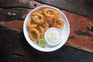 Kırsal ahşap masada izole edilmiş sos soslu kızarmış kalamar halkalarının üst görüntüsü.