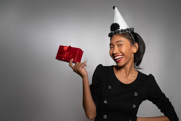 非常快乐的亚洲女孩 戴着生日帽 手里拿着灰色墙壁背景上的礼物 — 图库照片