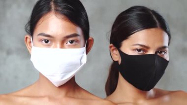 Yakın plan, tıbbi maske takmış iki güzel Asyalı kadının beton arka planda poz verişiyle karşılaşıyor. Coronavirus ve covid-19 konsepti