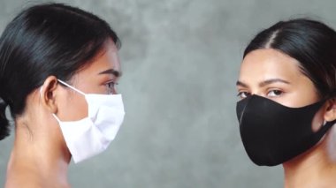 Yakın plan, tıbbi maske takmış iki güzel Asyalı kadının beton arka planda poz verişiyle karşılaşıyor. Coronavirus ve covid-19 konsepti
