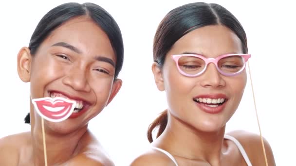 白い背景に小道具のメガネと唇でポーズをとっている2人の若い笑顔のアジアの女性の肖像画 パーティー 写真ブース 楽しい時間のコンセプト — ストック動画