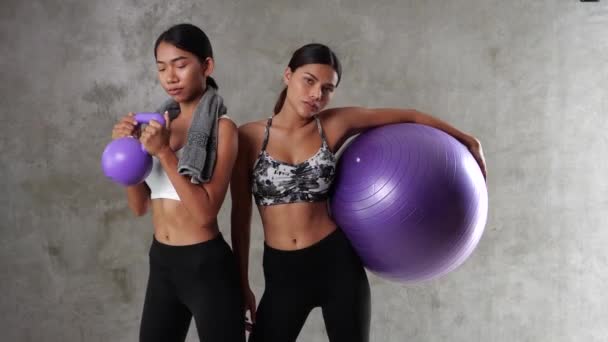 两名漂亮的年轻亚洲女子在体育馆摆出健康球和哑铃的姿势 快乐的女性朋友在体育中心度过了他们的闲暇时光 — 图库视频影像
