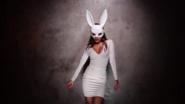 Beyaz elbiseli ve tavşan maskeli güzel Asyalı kadının portresi. Kamera önünde şakacı bir şekilde poz veriyor. Yavaş çekimde video.